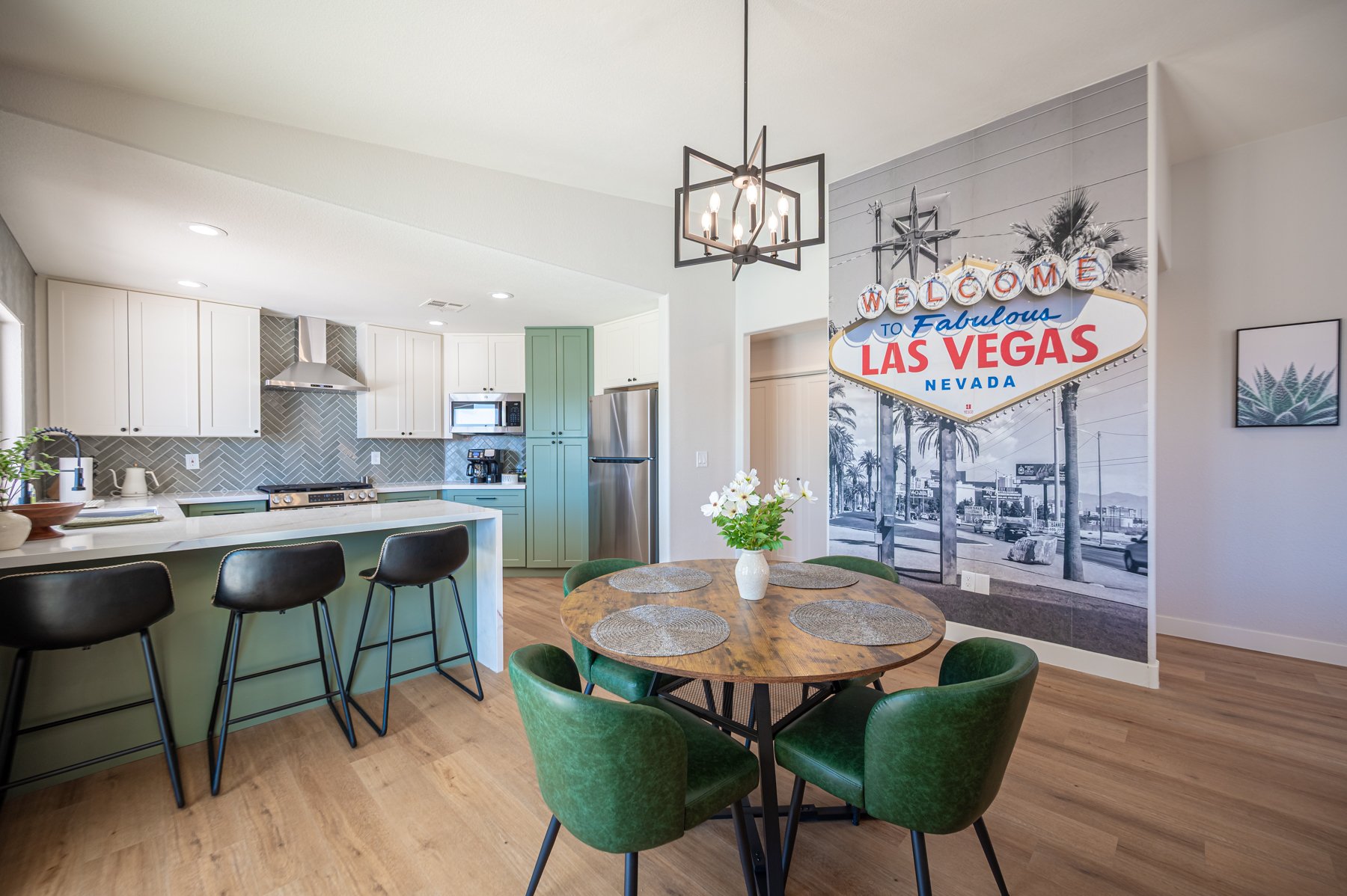 Modern Airbnb kitchen and dining area in Las Vegas with sage green island, velvet chairs, and vintage-style mural – Eleganti Design